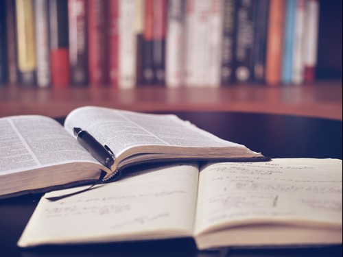 Books and notebook on a table with a bookshelf in the background